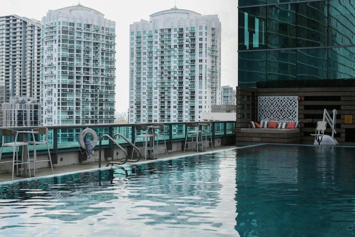 Ilustrai kolam renang rooftop hotel dengan pemandangan gedung-gedung kota.