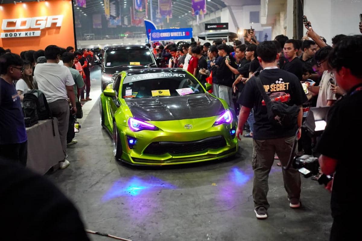 Mobil sport berwarna hijau metalik dengan modifikasi body kit dipamerkan di acara otomotif indoor yang ramai pengunjung.