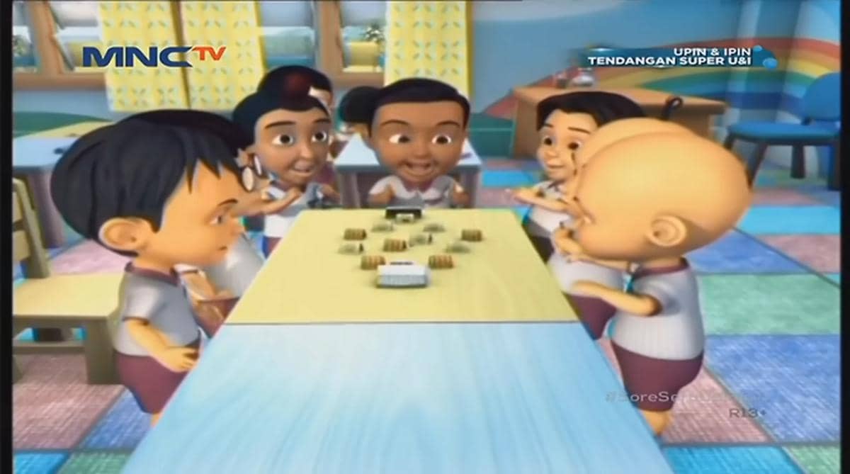 Karakter animasi anak-anak dari serial Upin Ipin duduk di meja kelas sambil bermain bersama di ruang belajar berwarna cerah.
