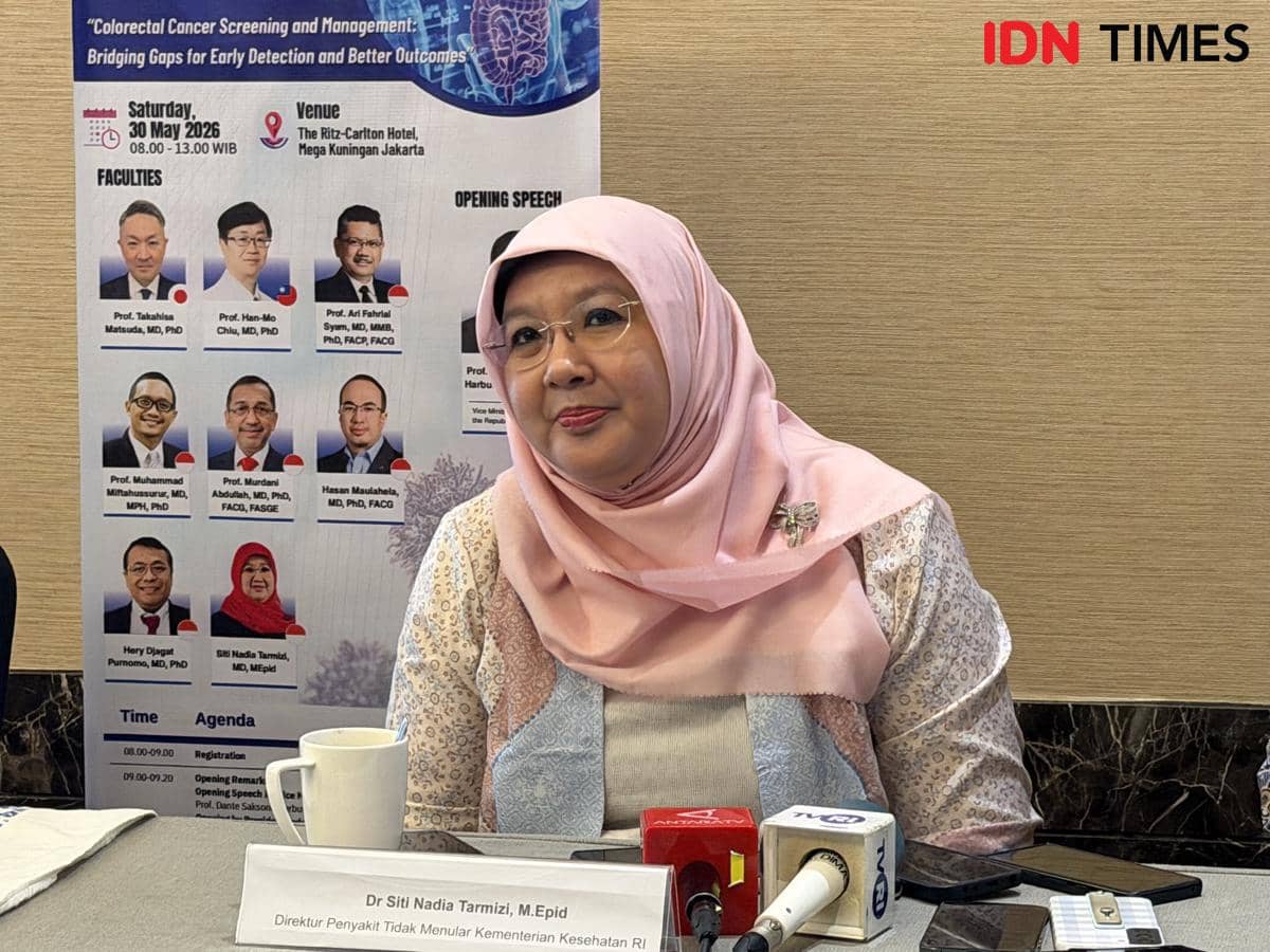 Seorang perempuan berhijab pink duduk di depan meja dengan mikrofon dan cangkir, berbicara dalam konferensi pers di Jakarta.