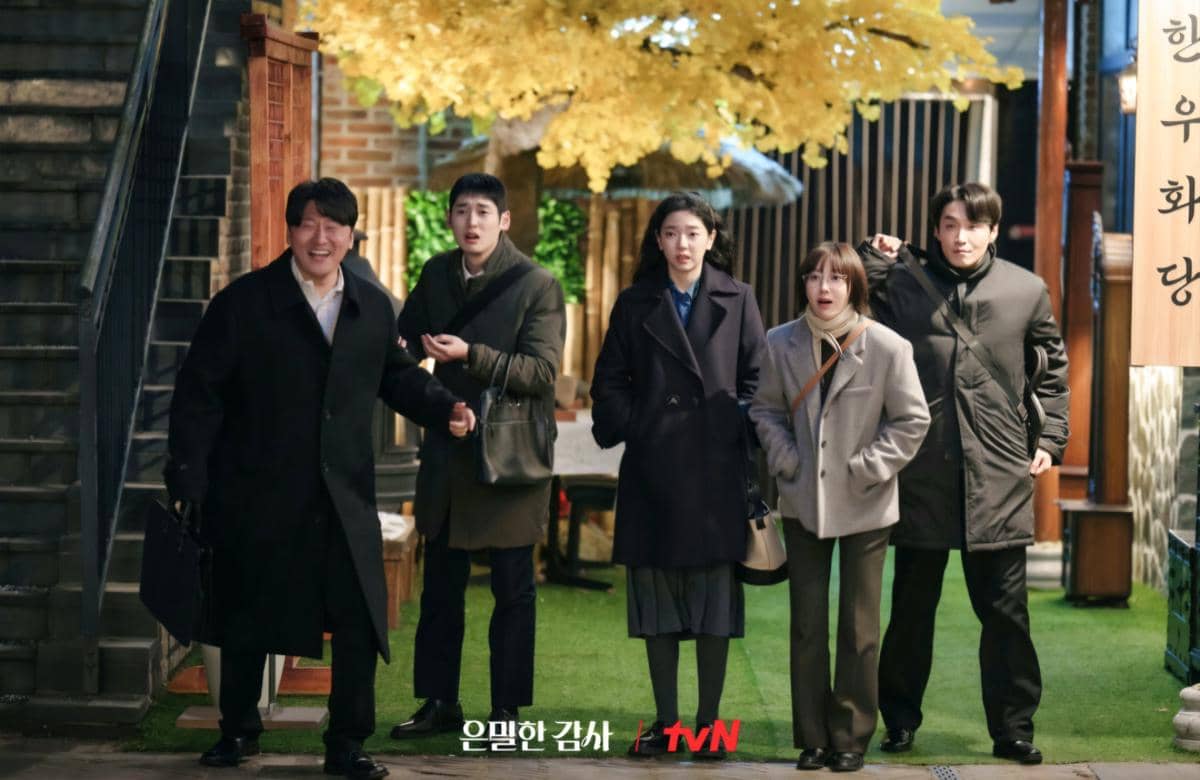 Lima orang berdiri di luar restoran dengan latar pohon berdaun kuning dalam cuplikan drama Korea Filing for Love dari tvN.