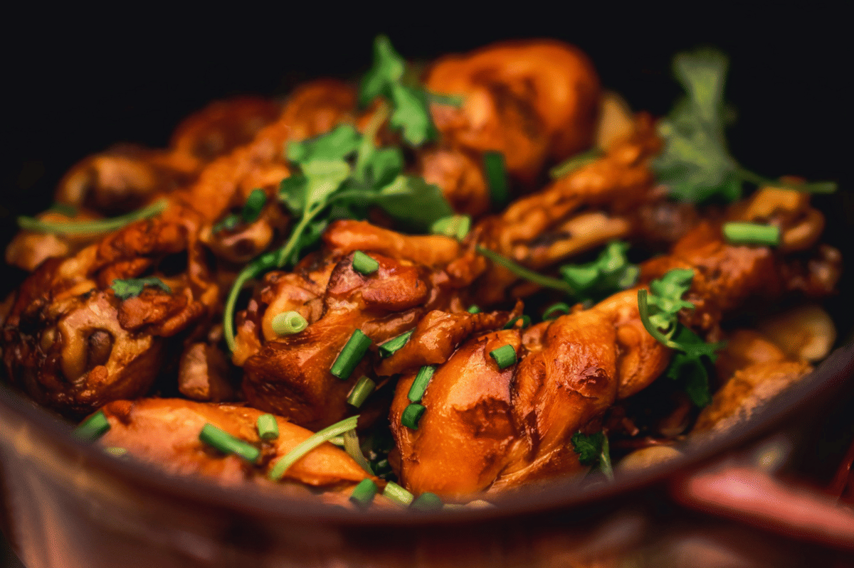 Hidangan poulet au vinaigre dengan potongan ayam berwarna kecokelatan, dihiasi daun ketumbar dan potongan daun bawang segar.