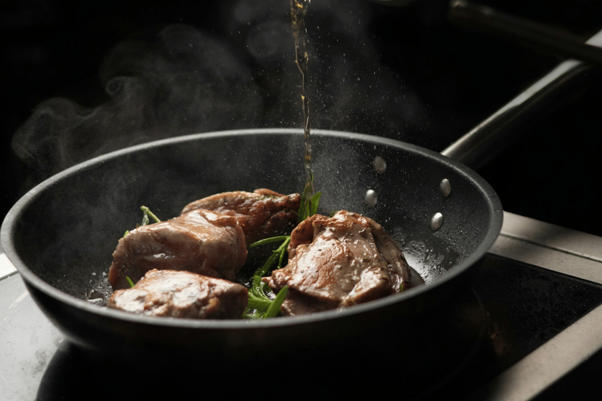Potongan daging ayam sedang dimasak dalam wajan dengan saus dan rempah segar untuk hidangan poulet au vinaigre khas Prancis.