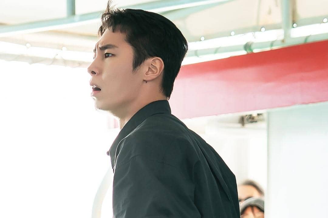 Seorang pria berambut pendek mengenakan kemeja gelap terlihat terkejut dalam adegan drama Doctor On The Edge.