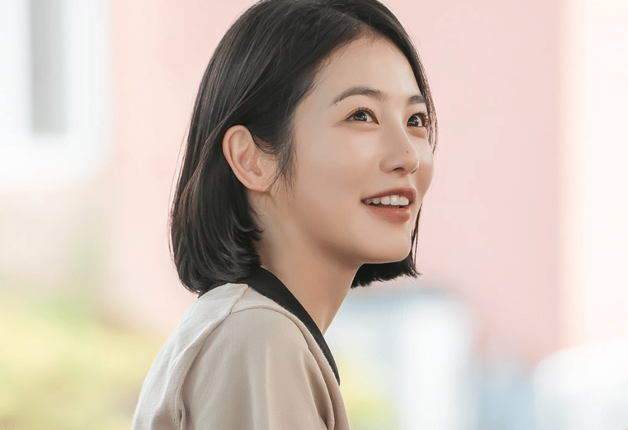 Seorang perempuan berambut pendek tersenyum cerah dalam cuplikan drama Korea Doctor On The Edge produksi ENA.
