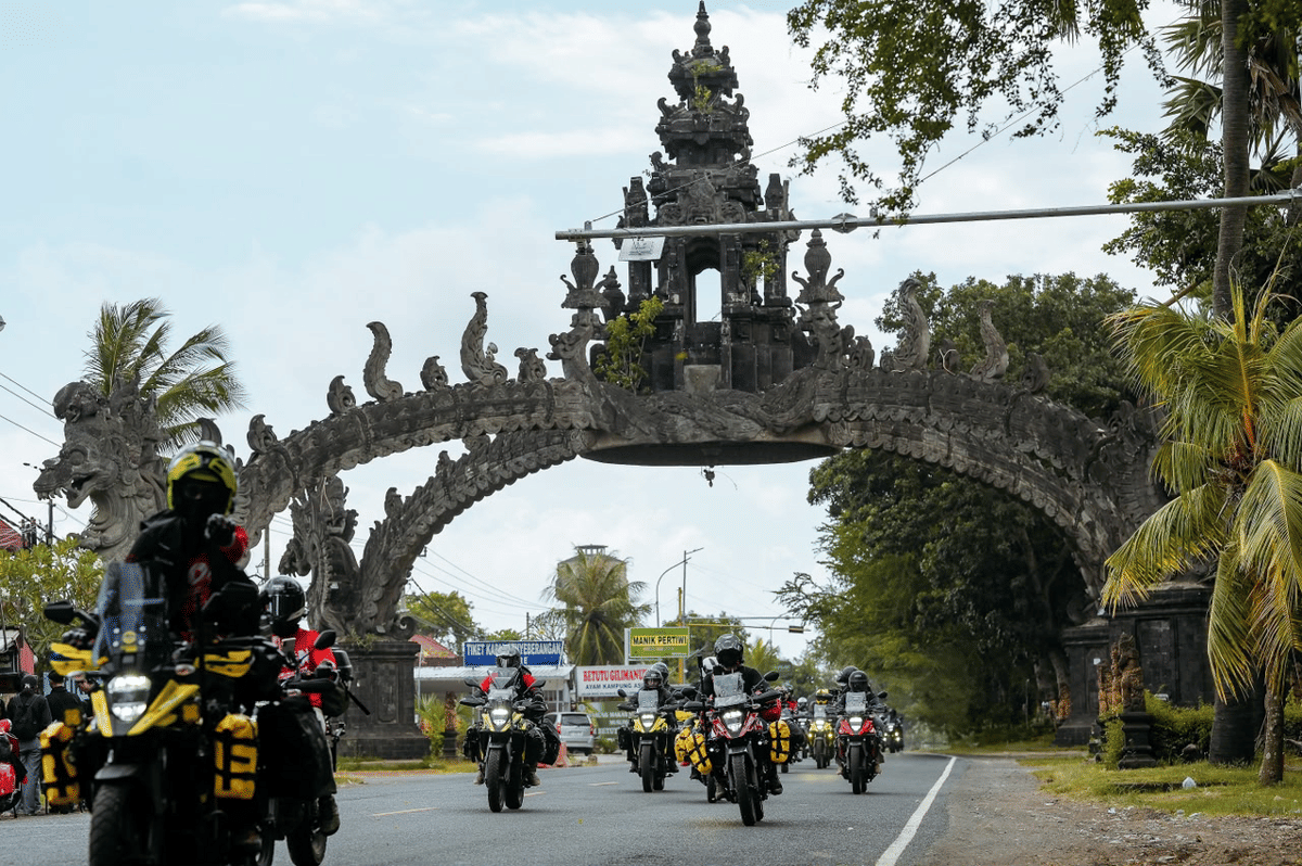 Rombongan pengendara motor Suzuki V-Strom 250SX melintasi gerbang bercorak khas Bali saat melakukan touring di jalan raya.