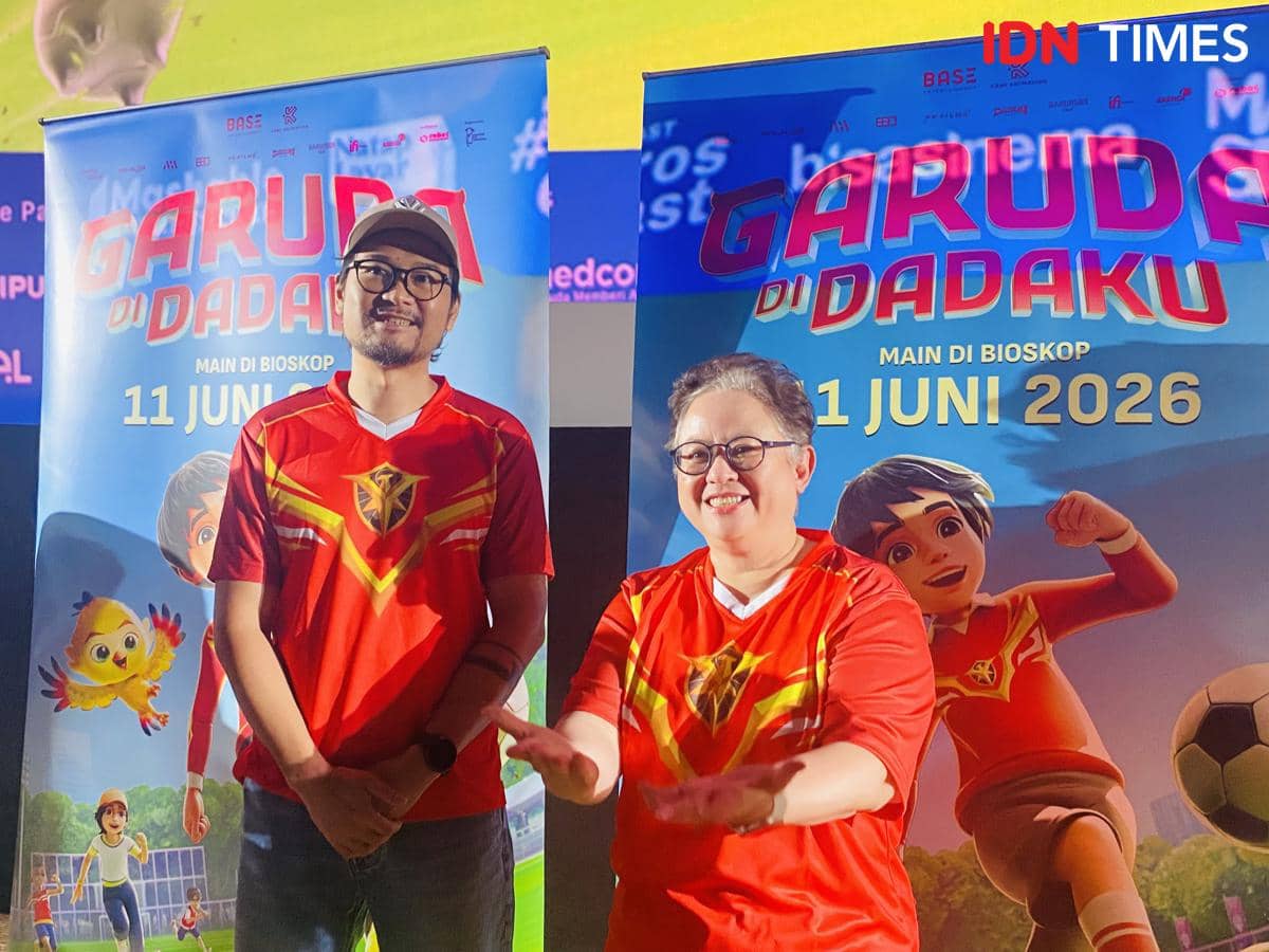 Dua orang mengenakan kaus merah bergambar logo Garuda berdiri di depan poster film animasi Garuda di Dadaku di XXI Epicentrum.