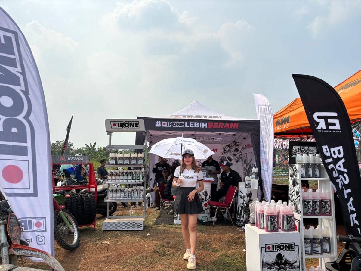 Stan IPONE dengan produk pelumas motor dan perlengkapan trail dipamerkan di area outdoor dengan beberapa pengunjung dan motor trail di sekitarnya.