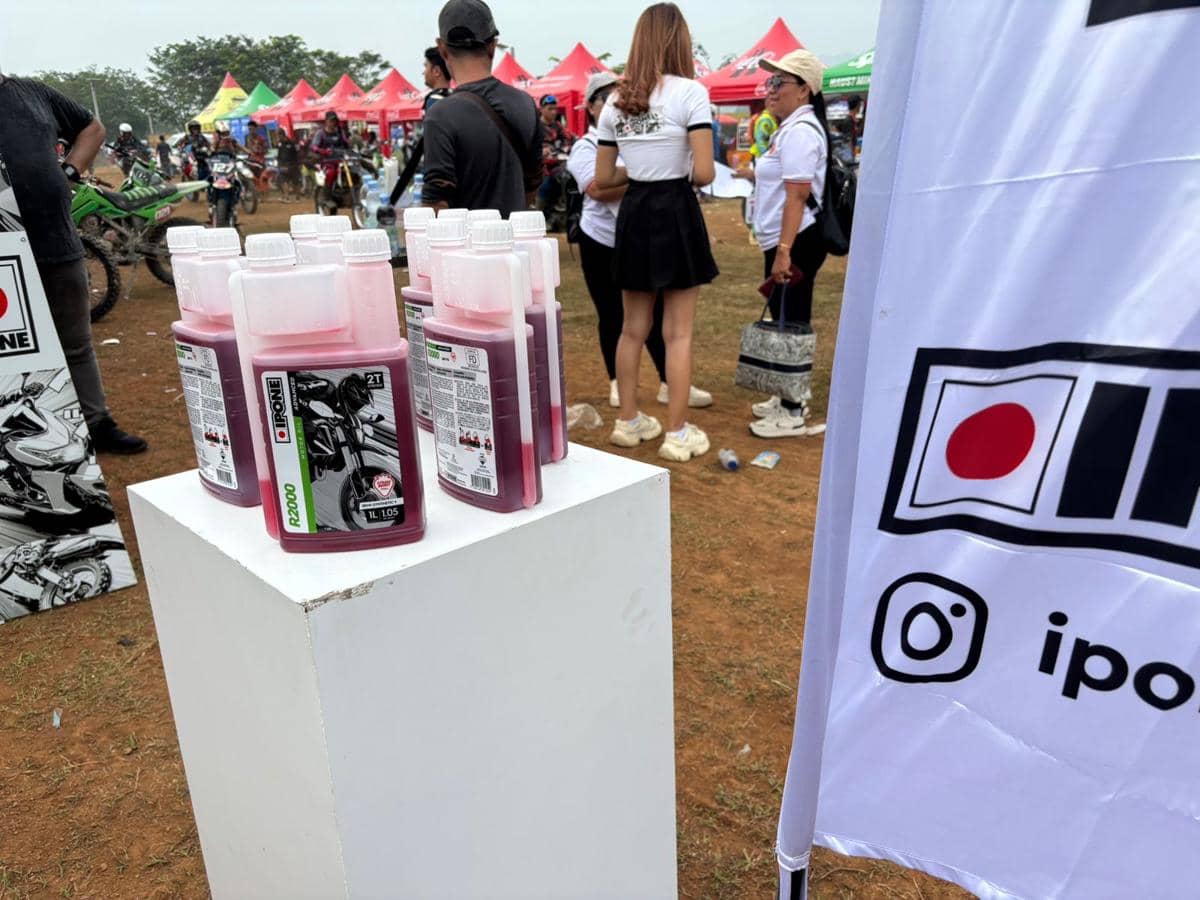 Beberapa botol pelumas mesin IPONE berwarna merah muda dipajang di atas podium putih pada acara otomotif luar ruangan.