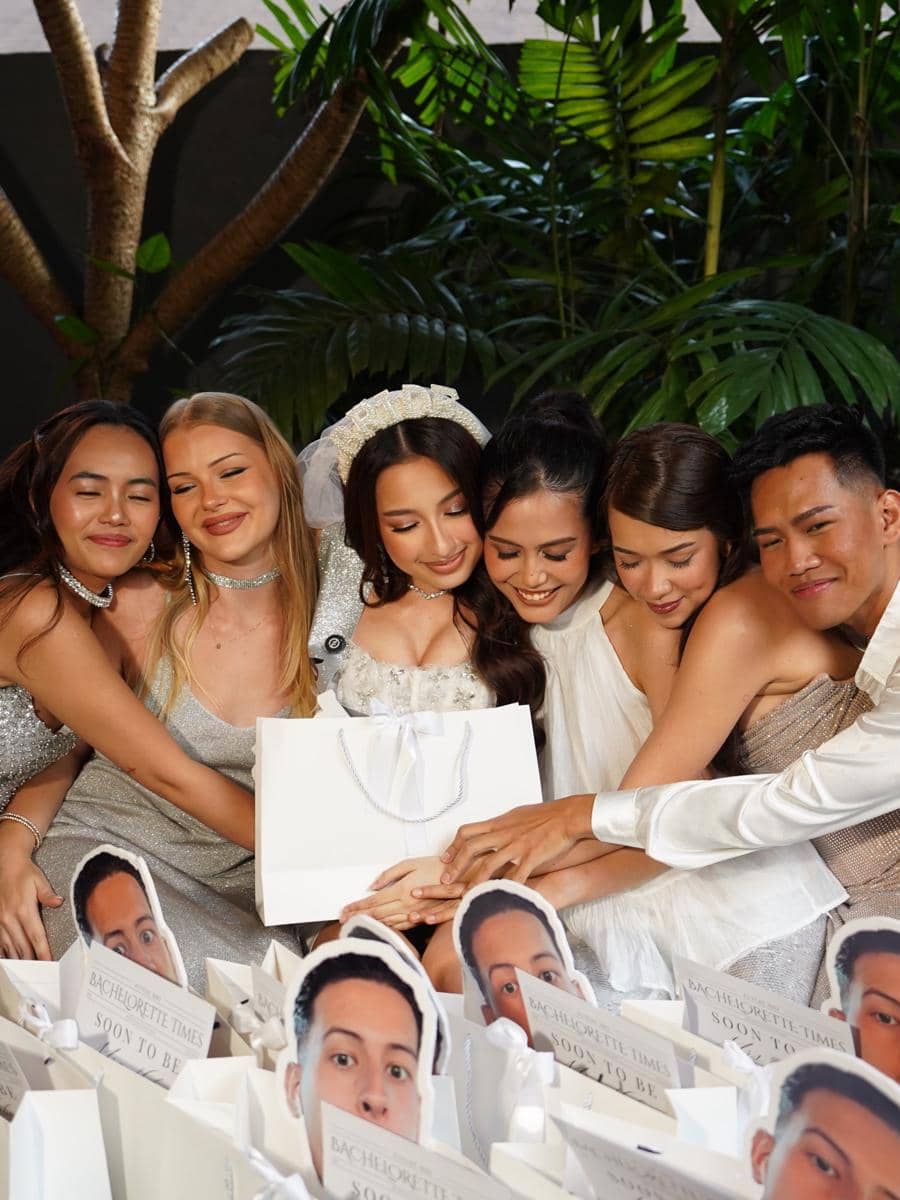 Sekelompok teman berpose bersama calon pengantin wanita dalam acara bridal shower dengan dekorasi tas hadiah putih di sekeliling mereka.