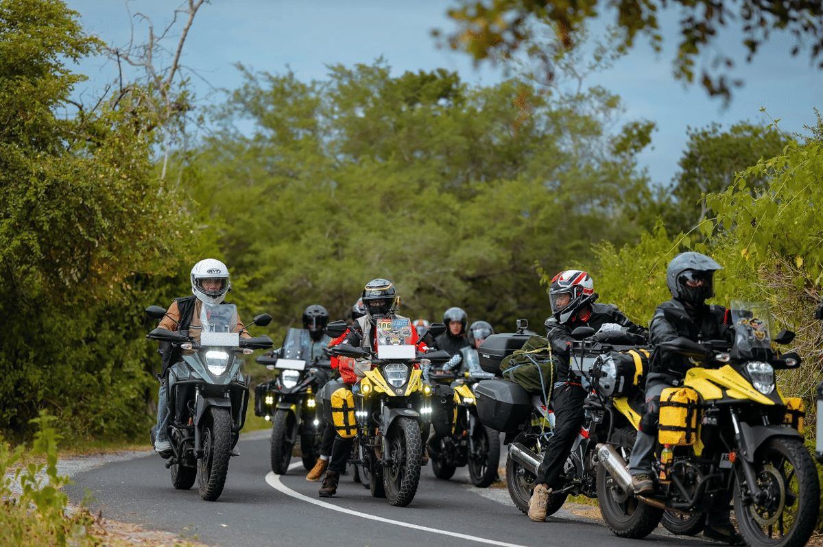 Sekelompok pengendara motor touring melintasi jalan berkelok di area hijau dengan perlengkapan lengkap dan motor tipe adventure.