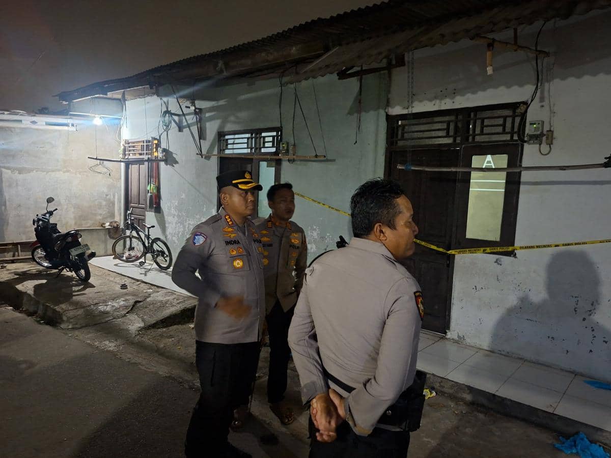 Beberapa polisi memeriksa lokasi kejadian perkara pembunuhan di depan rumah sederhana di Cikupa pada malam hari.