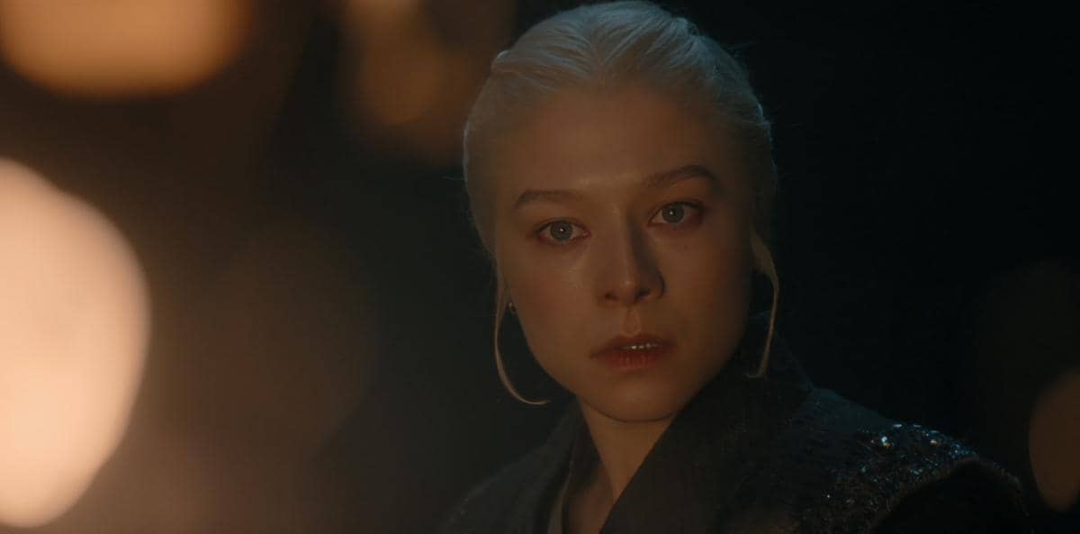 Seorang karakter berambut pirang pucat menatap serius dalam pencahayaan redup pada adegan serial House of the Dragon.