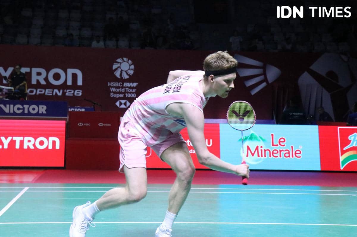 Seorang pemain bulu tangkis melakukan gerakan bertahan di lapangan saat pertandingan Indonesia Open 2026 dengan latar belakang papan sponsor.