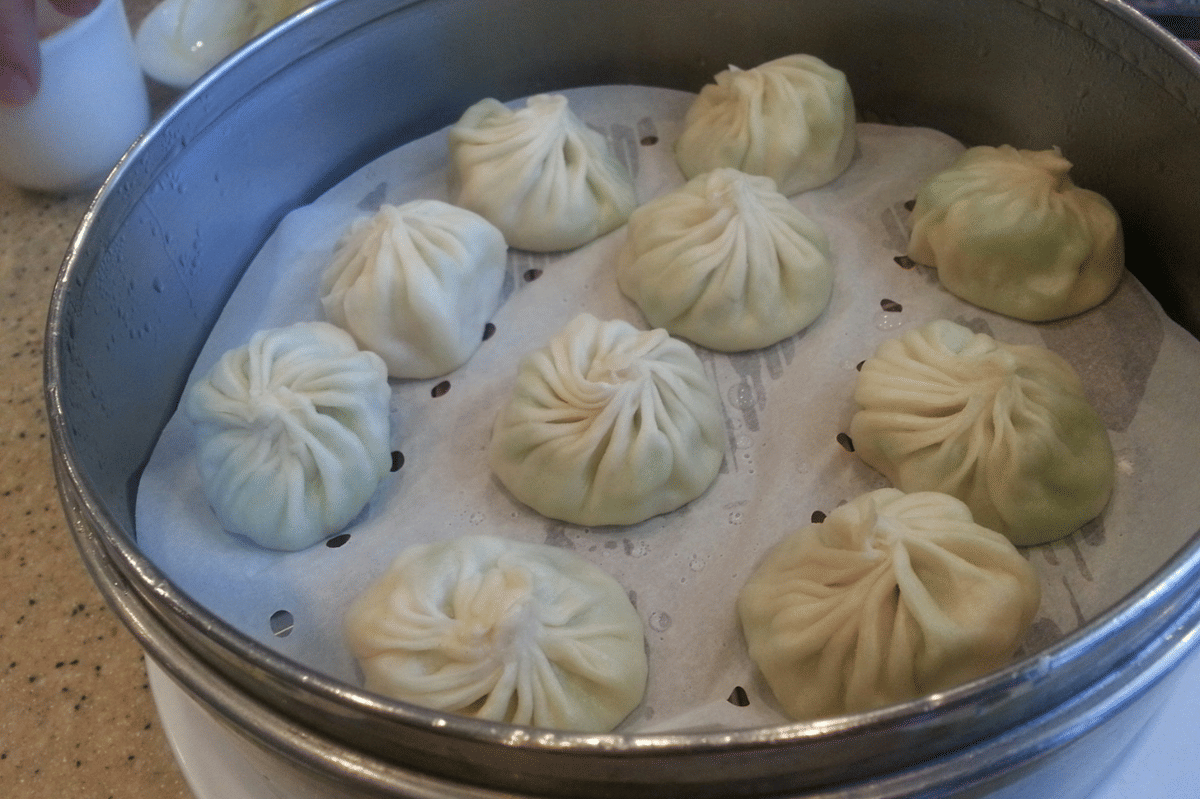 Beberapa xiao long bao kukus tersusun di dalam kukusan logam dengan alas kertas berlubang di atas meja dapur.