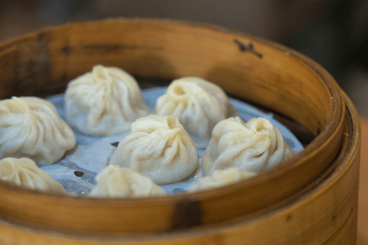 Beberapa xiao long bao kukus tersusun rapi di dalam kukusan bambu dengan kulit lembut dan lipatan khas di bagian atas.