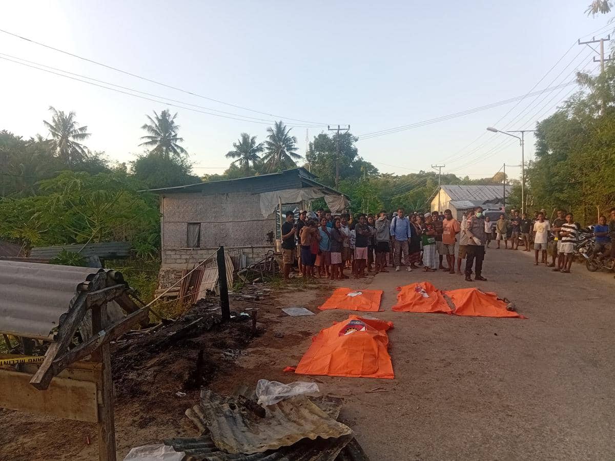 Petugas dan warga berkumpul di dekat pondok yang terbakar di Sumba Timur dengan empat kantong jenazah berwarna oranye di jalan.