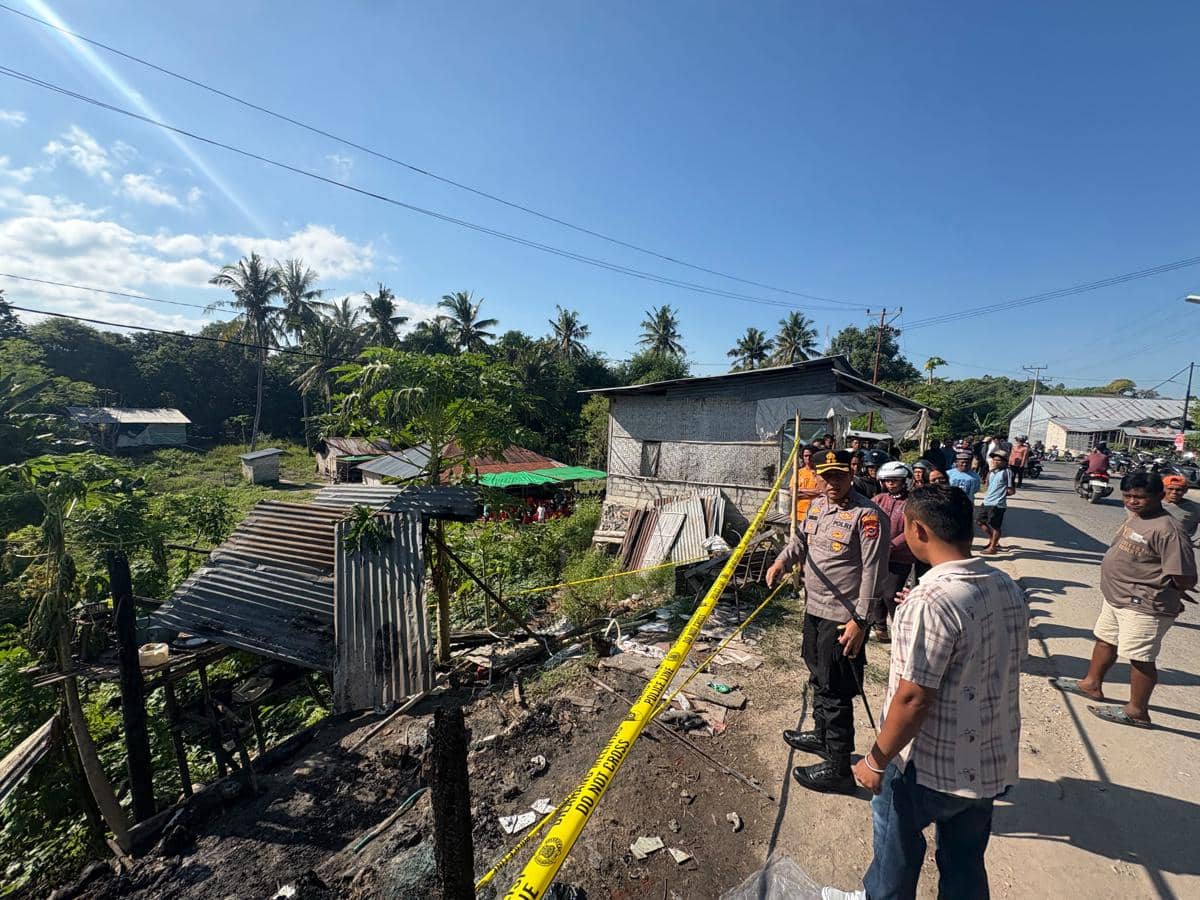 Petugas kepolisian memeriksa lokasi kebakaran pondok di Sumba Timur yang dipasangi garis polisi dengan warga sekitar menyaksikan.