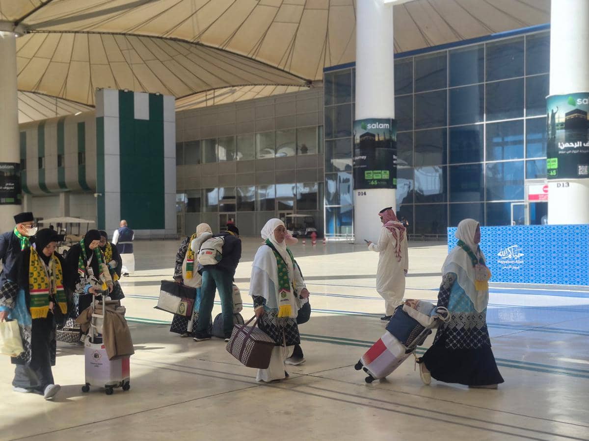 Jemaah haji Indonesia mengenakan pakaian ihram dan syal hijau berjalan membawa koper di Bandara Internasional King Abdulaziz Jeddah.