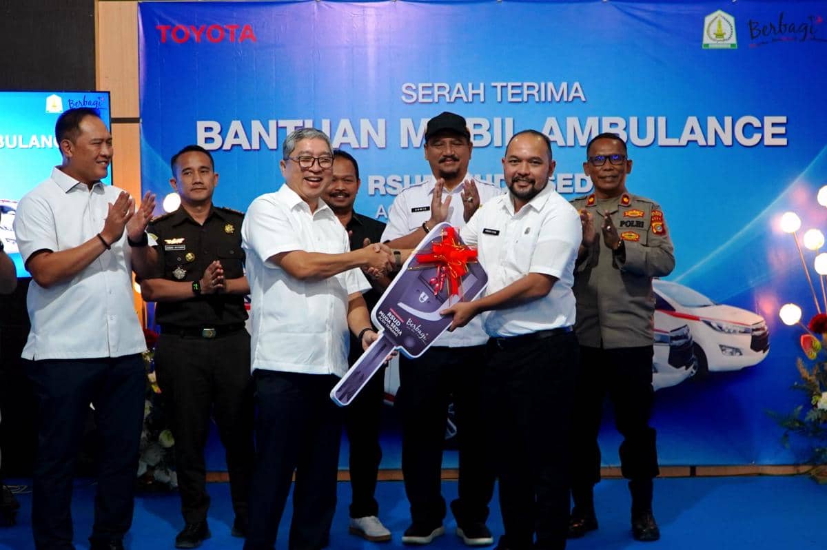 Beberapa pejabat berfoto bersama saat serah terima bantuan mobil ambulans, dua orang di depan berjabat tangan sambil memegang replika kunci besar.