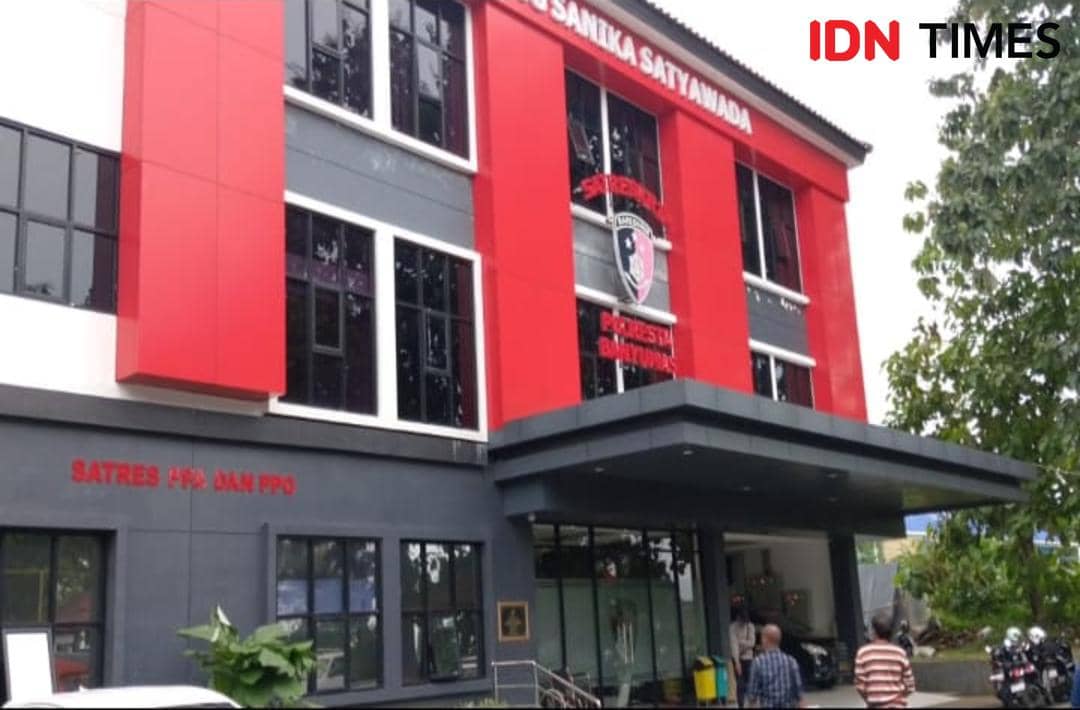 Gedung Polresta Banyumas dengan dinding merah dan abu-abu tampak dari luar, beberapa orang berdiri di area depan gedung.