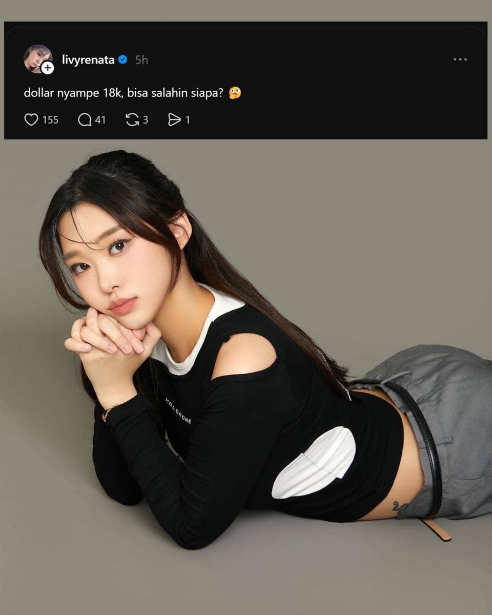 Seorang perempuan berpose berbaring dengan tangan terlipat di depan wajah, mengenakan atasan hitam dan celana abu-abu di latar polos.