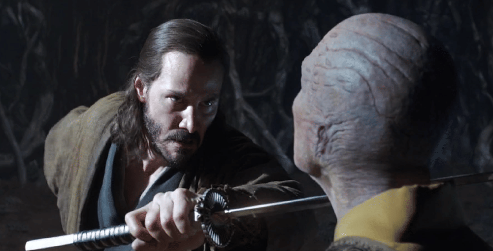Seorang pria memegang pedang dan menatap tajam ke arah sosok berkepala botak dengan kulit bertekstur aneh dalam adegan film 47 Ronin.