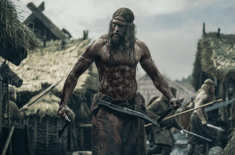 Seorang pria bertubuh kekar berlumuran darah memegang kapak di tengah desa bergaya Viking dengan latar rumah beratap jerami.