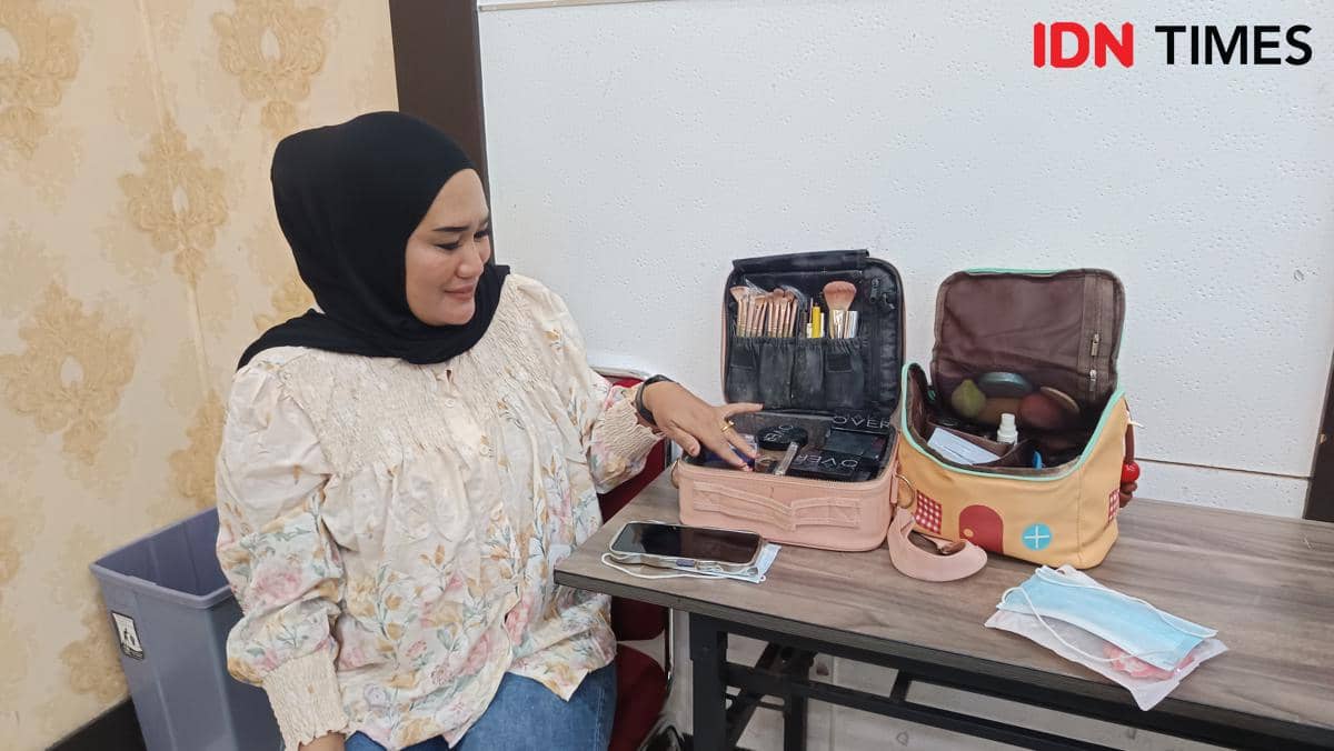 Seorang wanita berhijab duduk di meja sambil memperlihatkan perlengkapan rias seperti kuas dan kosmetik di Asrama Haji Sudiang, Makassar.