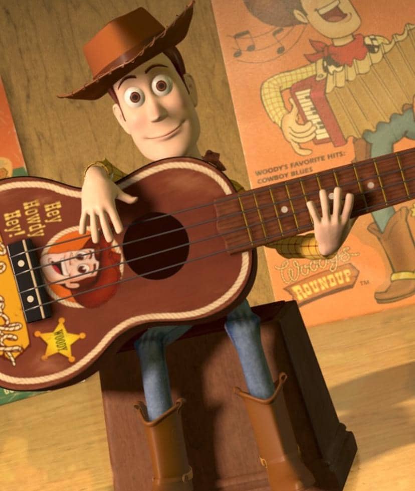Karakter animasi koboi mengenakan topi cokelat sedang memainkan gitar kayu besar dengan latar poster bergaya vintage di dinding.