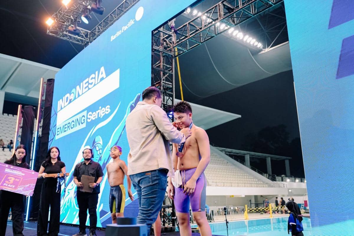 Seorang perenang muda menerima medali di podium penghargaan Indonesia Short Course Emerging Series 2026 di kolam renang indoor.
