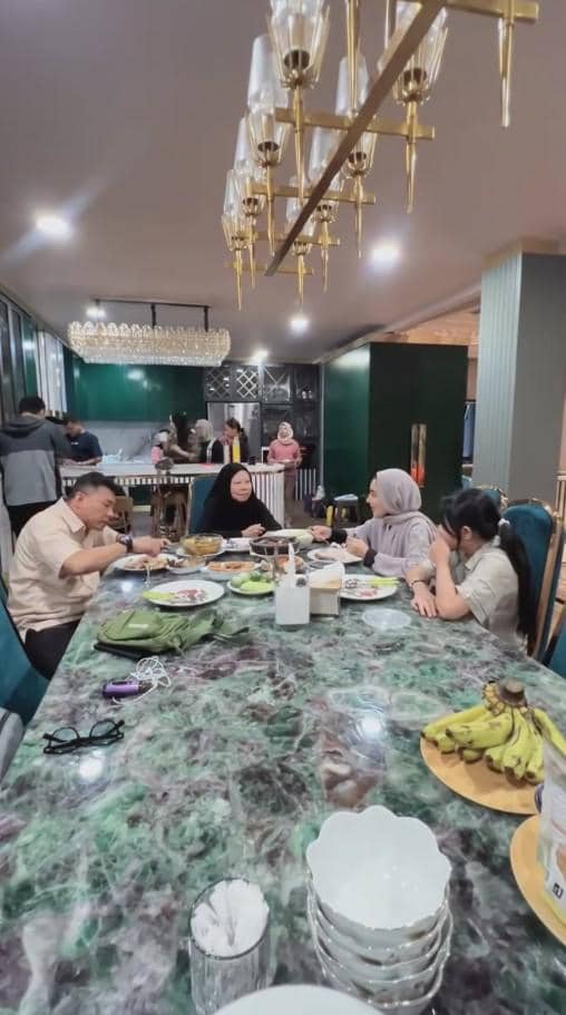 Beberapa orang duduk di meja makan besar dengan hidangan lengkap di ruang makan modern setelah pulang dari ibadah haji.