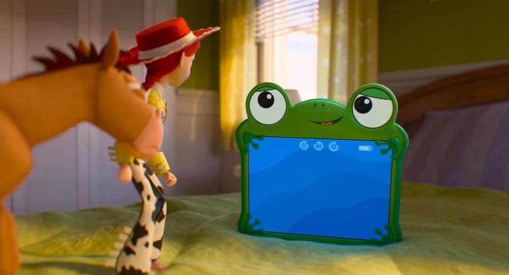 Karakter mainan koboi dan kuda melihat tablet berbentuk katak di atas tempat tidur dalam cuplikan film animasi Toy Story 5.