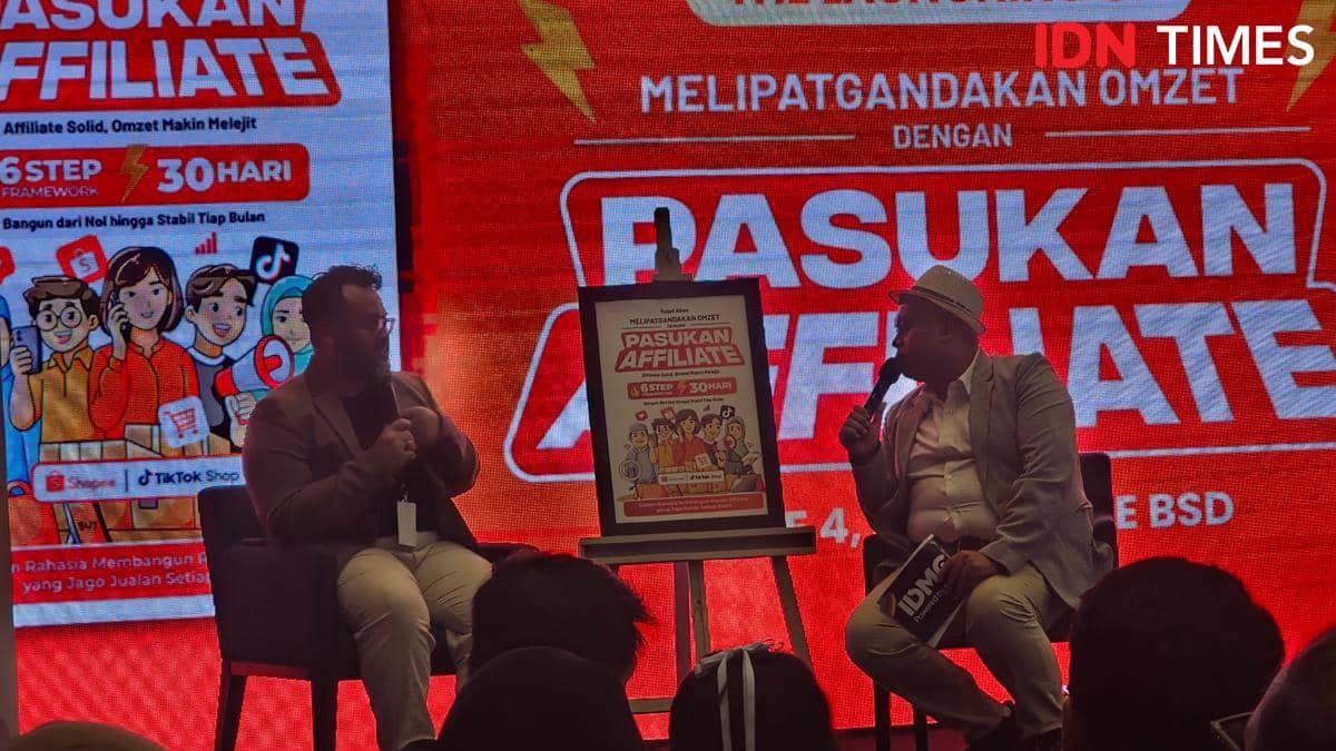 Dua pria berbincang di atas panggung saat peluncuran buku Pasukan Affiliate di ICE BSD, dengan latar belakang layar merah besar.