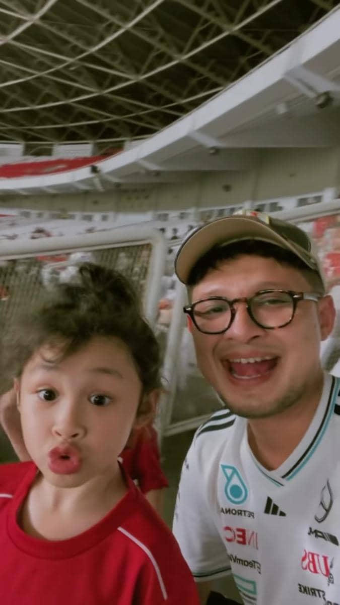 Seorang pria dan anak kecil berpose ceria di tribun stadion saat menonton pertandingan timnas Indonesia melawan Oman.