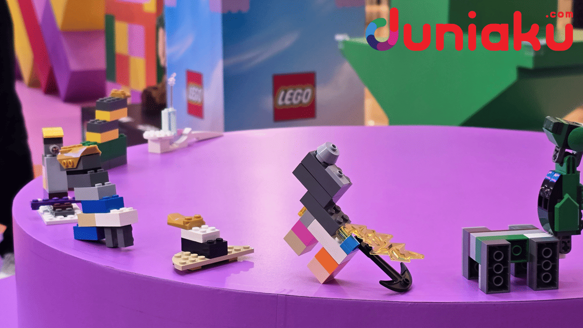 Beberapa kreasi LEGO berwarna-warni dipajang di meja ungu di area LEGO Playground dengan latar dekorasi cerah dan logo LEGO.