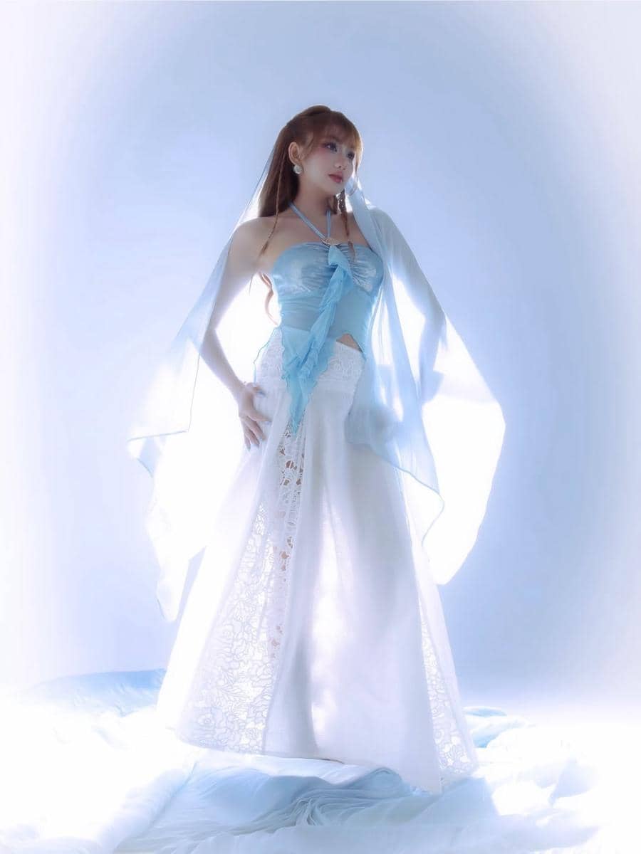 Seorang perempuan mengenakan gaun biru muda dan putih bergaya elegan dengan latar pencahayaan lembut bernuansa biru.