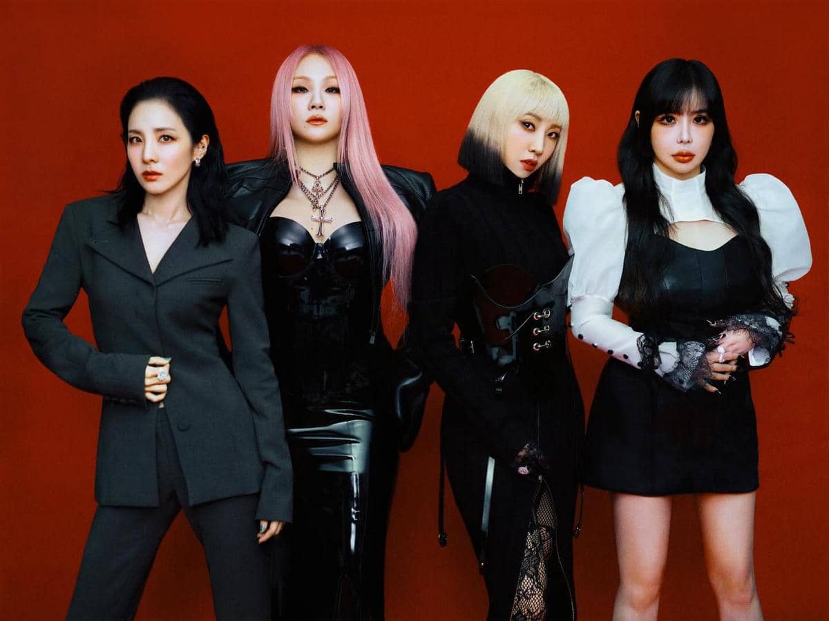 Empat wanita berdiri berpose di depan latar merah dengan busana hitam bergaya elegan dan ekspresi percaya diri.