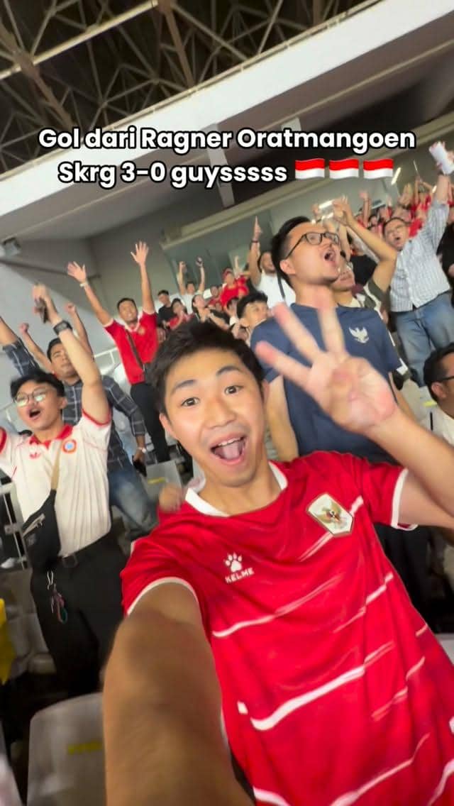 Seorang penonton bersorak gembira di stadion mengenakan jersey merah timnas Indonesia bersama suporter lain yang ikut merayakan kemenangan.