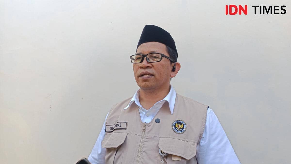 Seorang pria mengenakan peci hitam, kacamata, dan rompi berlogo Kementerian Haji dan Umrah berbicara di Asrama Haji Sudiang, Makassar.