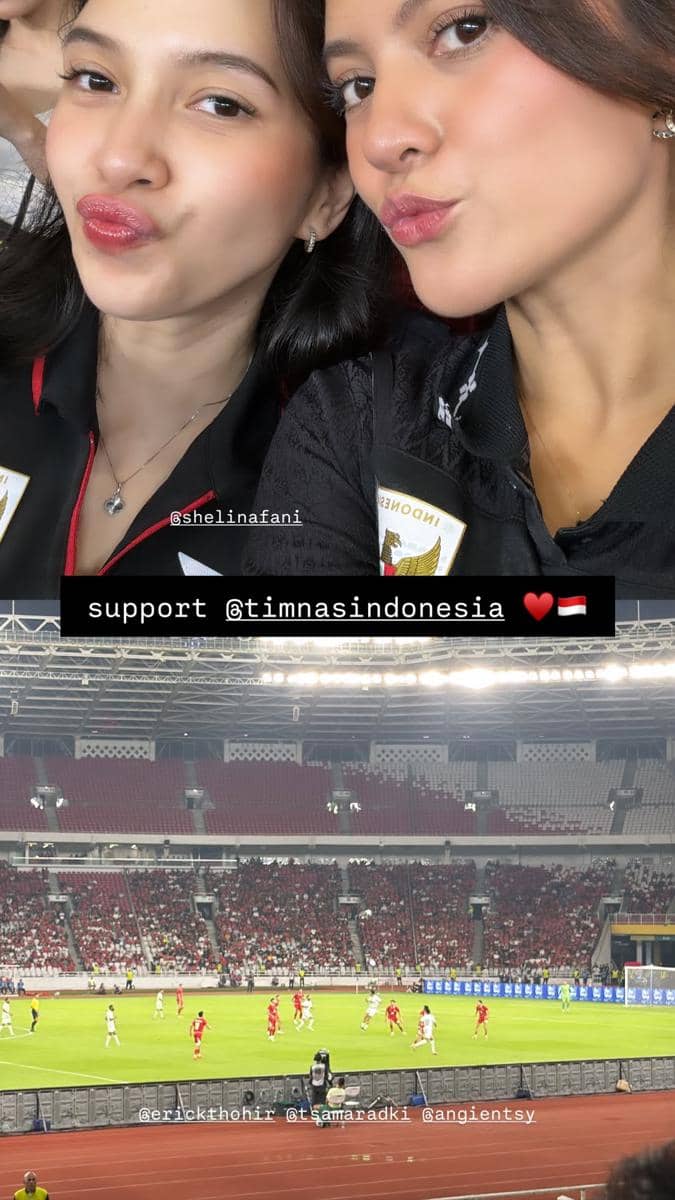 Dua perempuan mengenakan jersey hitam timnas Indonesia berpose di stadion saat menonton pertandingan Indonesia melawan Oman.