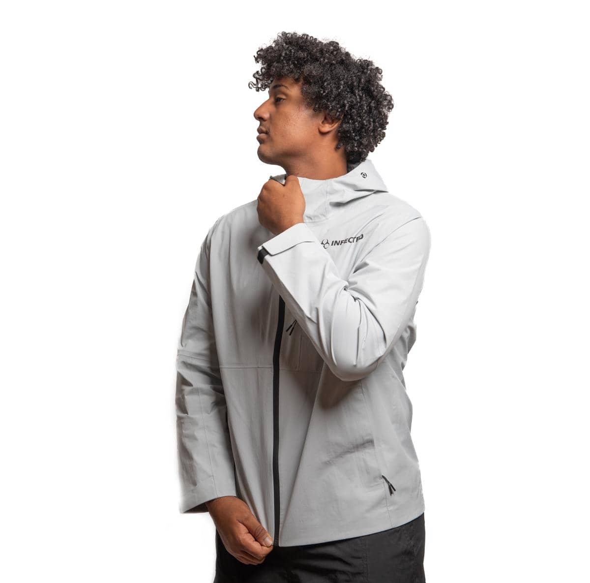 Seorang pria mengenakan jaket windbreaker abu-abu dengan ritsleting hitam, berdiri menghadap ke samping di latar belakang putih.