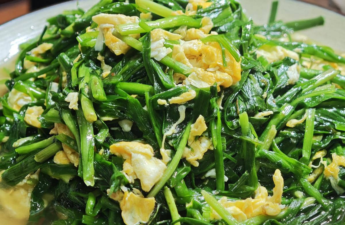 Tumis kangkung dengan potongan telur orak-arik berwarna kuning keemasan tersaji di atas piring, tampak segar dan menggugah selera.