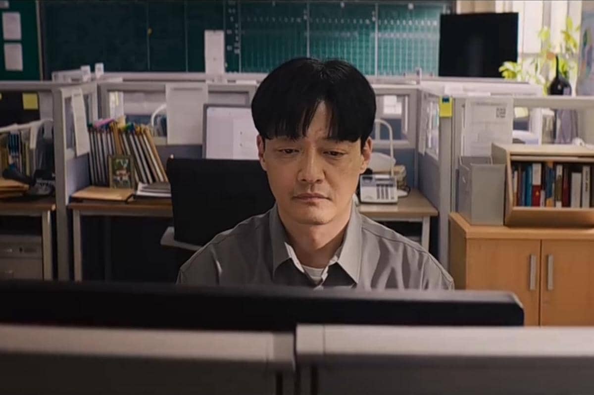 Seorang pria duduk di depan komputer di ruang kantor dengan suasana serius, diambil dari adegan serial Teach You a Lesson.