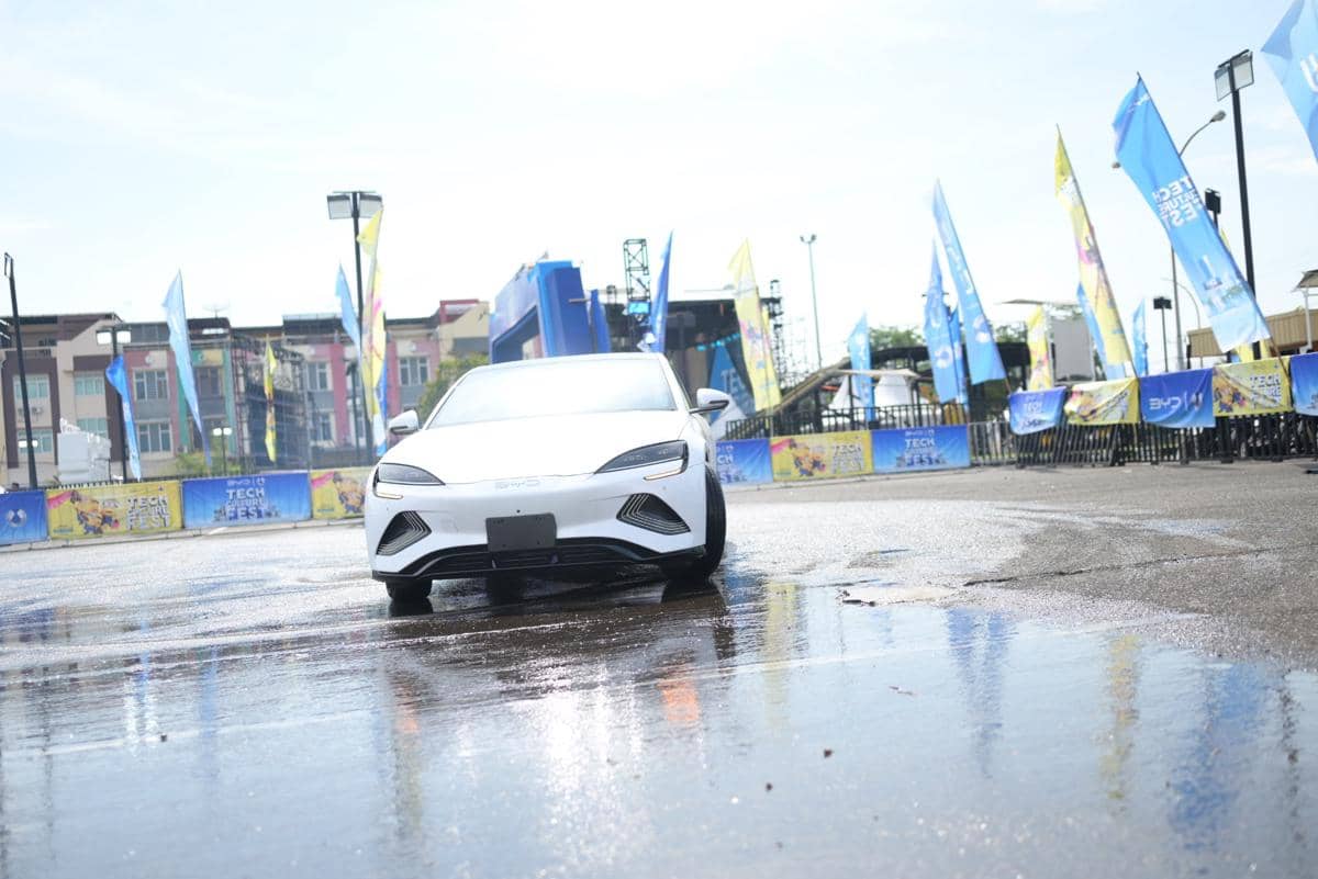 Mobil listrik BYD berwarna putih melaju di area uji coba saat acara BYD Tech Culture Fest 2026 di Medan dengan latar bendera promosi.