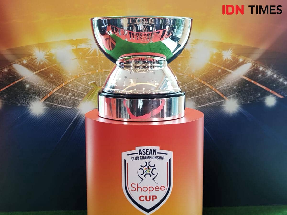 Piala ASEAN Club Championship Shopee Cup berwarna perak dipajang di atas podium merah dengan latar stadion bercahaya.