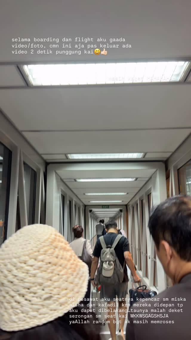 Penumpang berjalan di lorong menuju pesawat dengan membawa tas dan koper, suasana bandara terlihat sibuk dan terang.