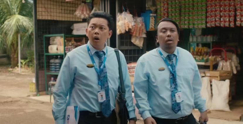 Dua pria mengenakan seragam biru muda dengan dasi bermotif berdiri di depan toko kelontong, tampak terkejut melihat sesuatu.