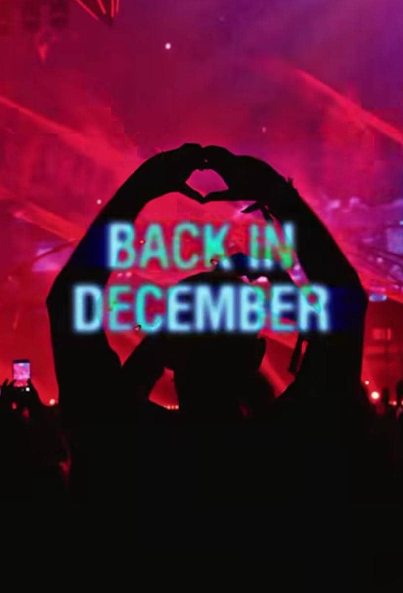 Siluet penonton membentuk simbol hati dengan tangan di konser musik berlampu merah dengan teks bercahaya 'Back in December'.