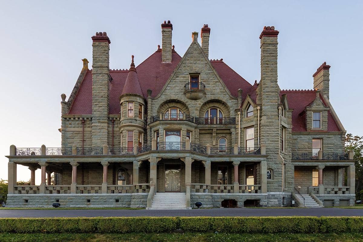 Bangunan megah Craigdarroch Castle bergaya Victoria dengan dinding batu abu-abu dan atap merah di bawah langit cerah.